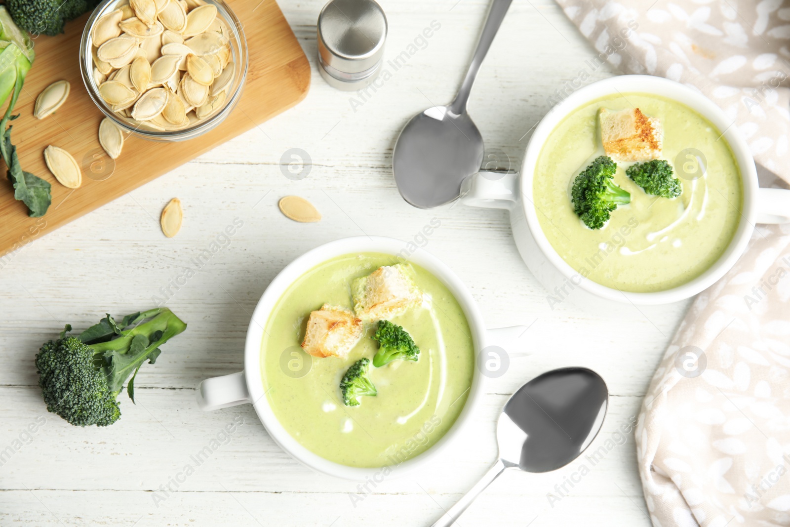 Photo of Delicious broccoli cream soup with croutons served on white wooden table, flat lay