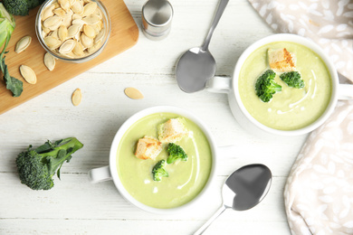 Photo of Delicious broccoli cream soup with croutons served on white wooden table, flat lay