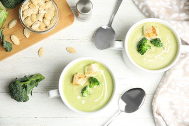 Delicious broccoli cream soup with croutons served on white wooden table, flat lay