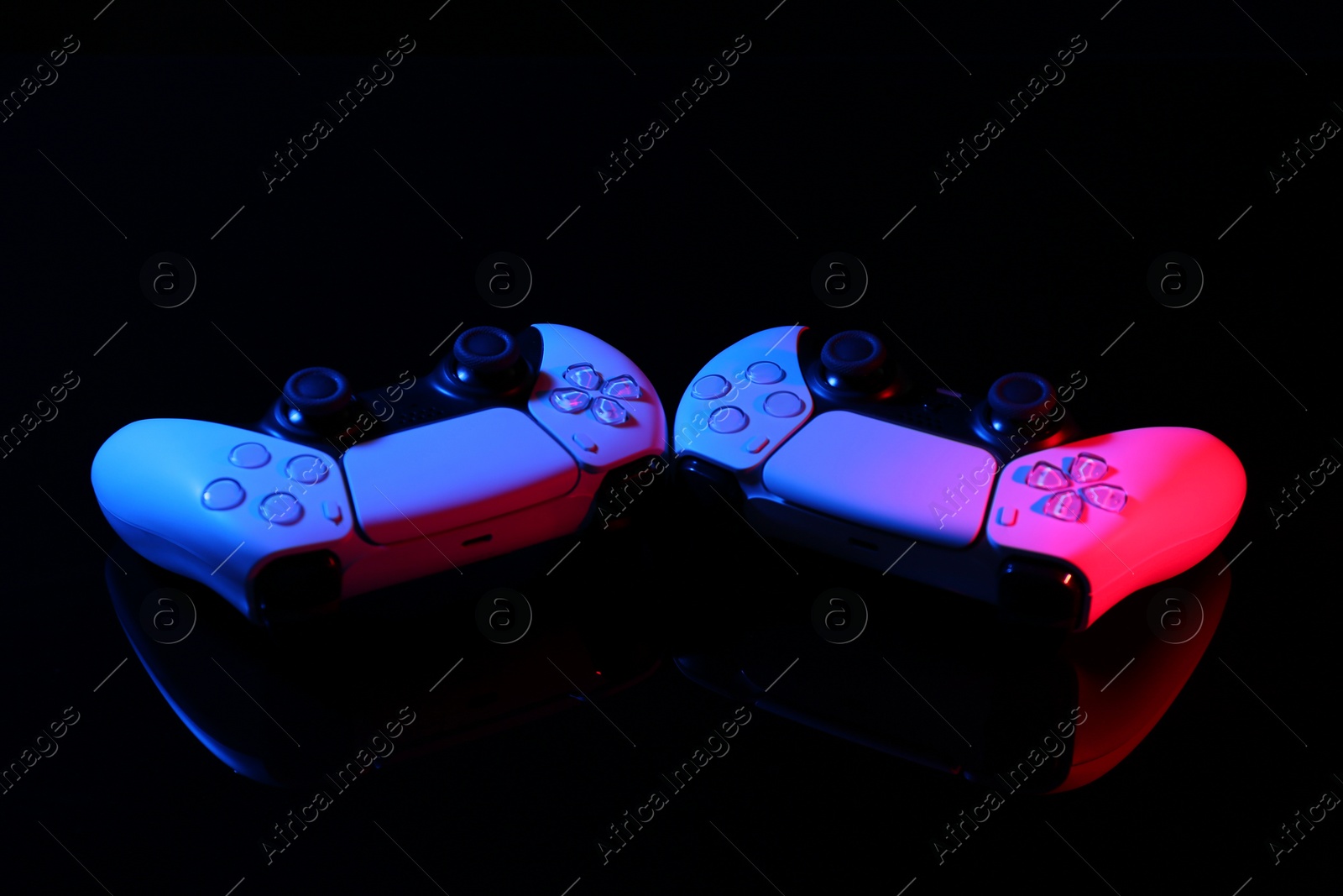 Photo of Wireless game controllers on black mirror surface in neon lights