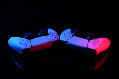 Photo of Wireless game controllers on black mirror surface in neon lights