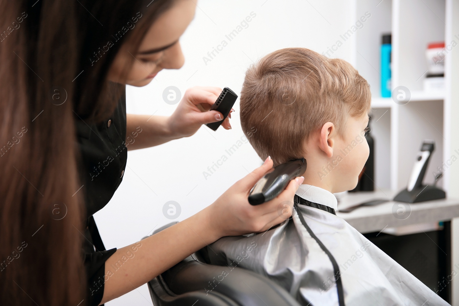 Photo of Professional female hairdresser working with little boy in salon