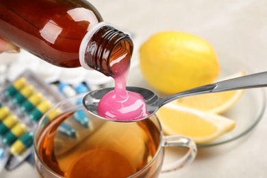 Photo of Pouring cough syrup from bottle into spoon on blurred background, closeup