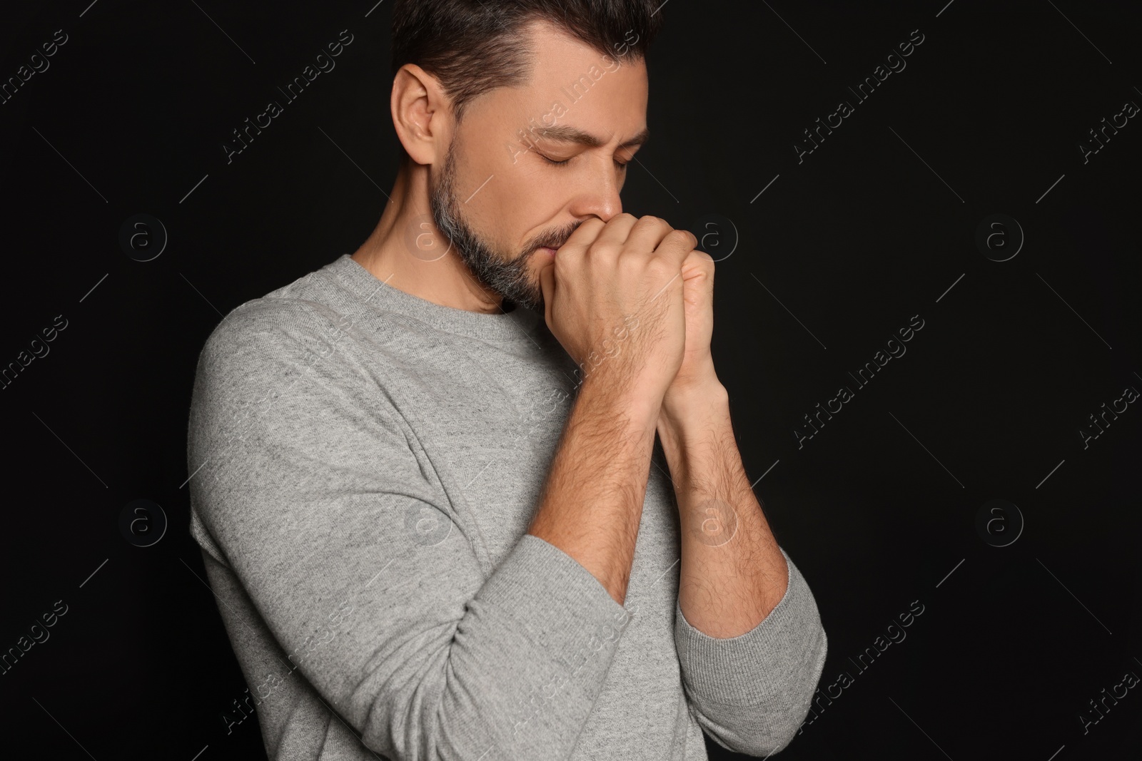 Photo of Man with clasped hands praying on black background