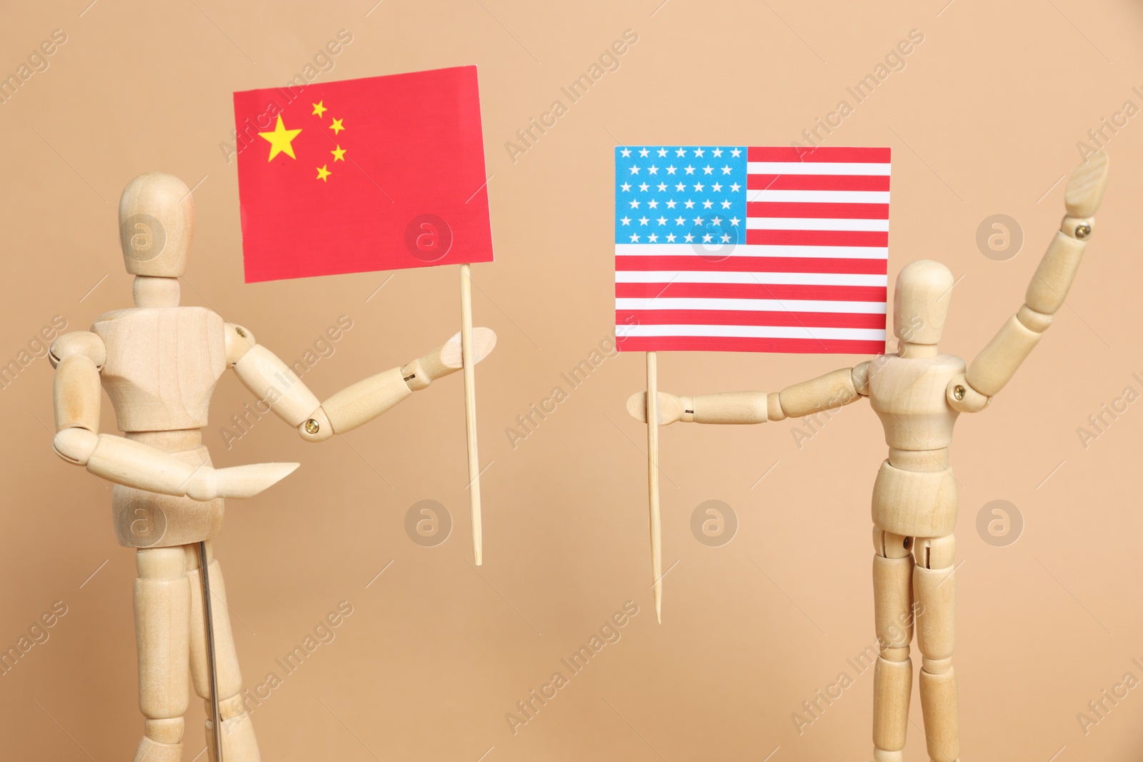 Photo of Wooden mannequins holding American and Chinese flags on beige background. Trade war