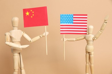 Photo of Wooden mannequins holding American and Chinese flags on beige background. Trade war