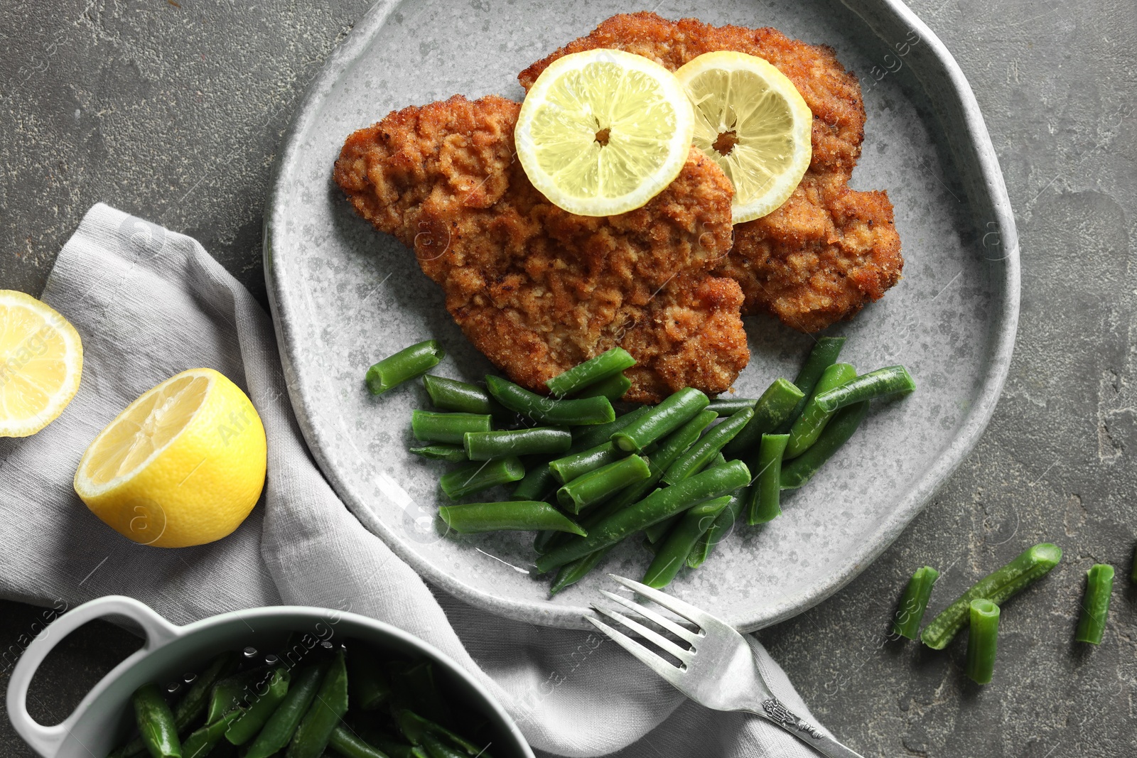 Photo of Tasty schnitzels served with lemon and green beans on grey table, flat lay