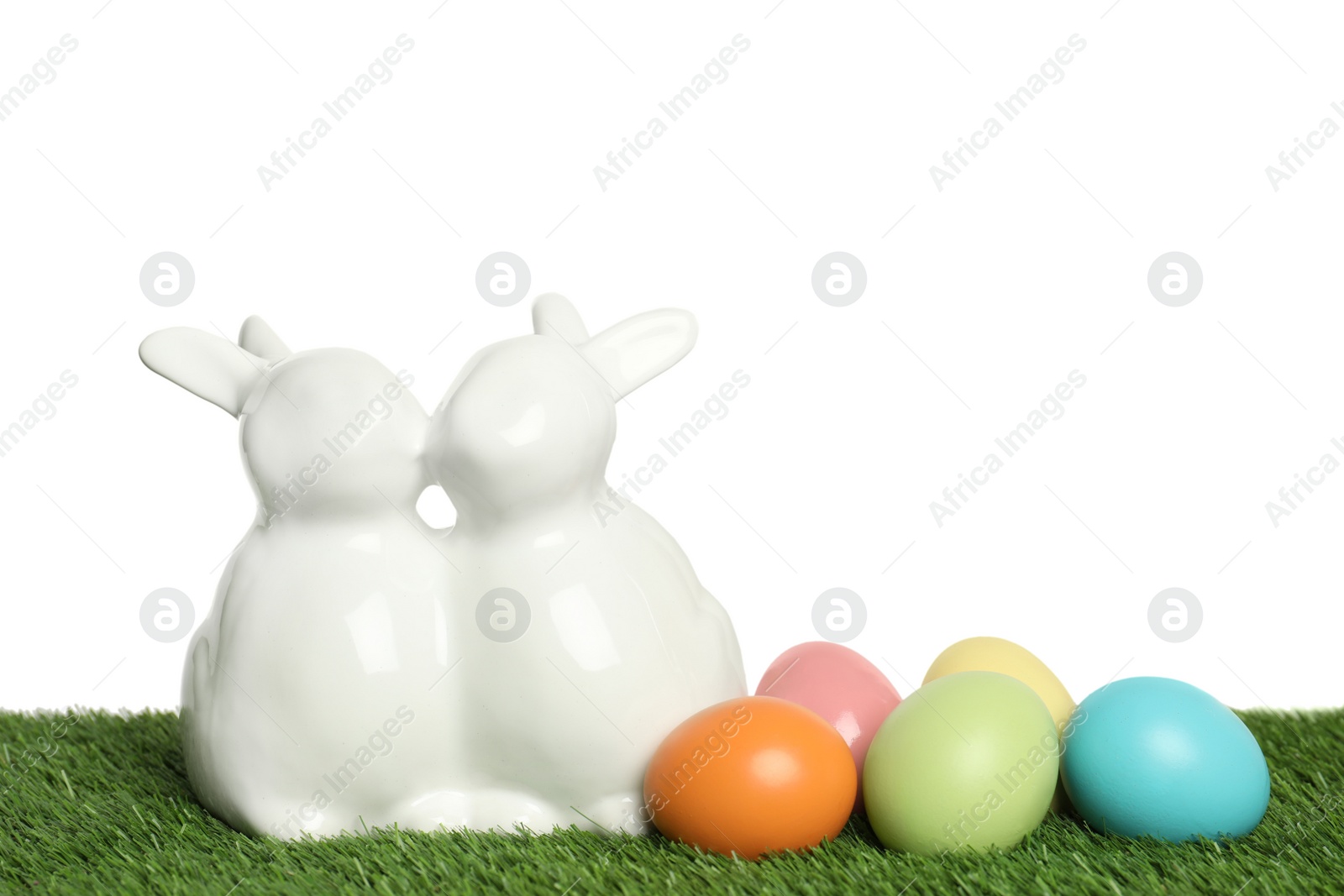 Photo of Ceramic Easter bunnies and dyed eggs on green grass against white background, space for text