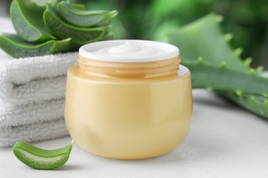 Jar with cream, cut aloe leaves and towel on white table against blurred green background, closeup