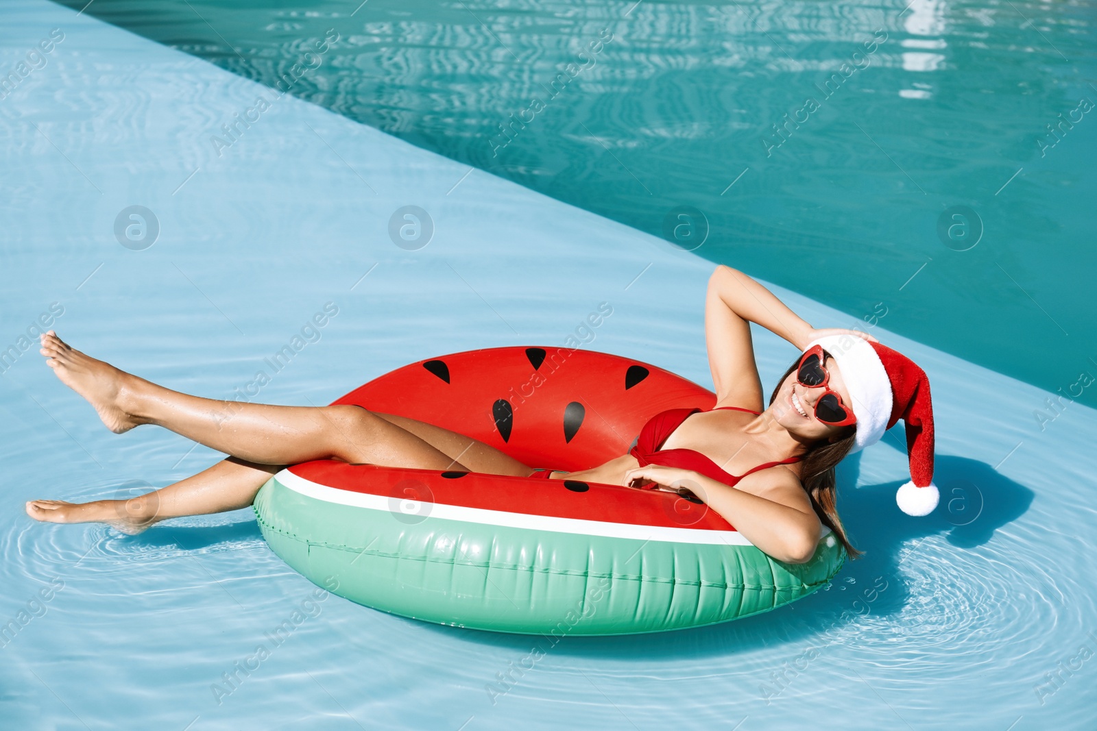 Photo of Young woman wearing Santa Claus hat on inflatable ring in swimming pool. Christmas vacation