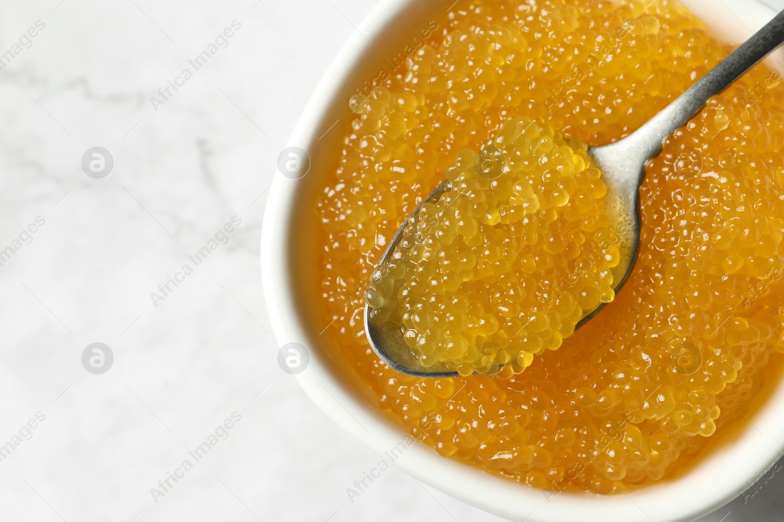 Photo of Fresh pike caviar in bowl and spoon on white marble table, top view. Space for text