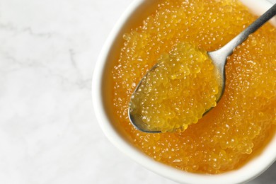 Photo of Fresh pike caviar in bowl and spoon on white marble table, top view. Space for text