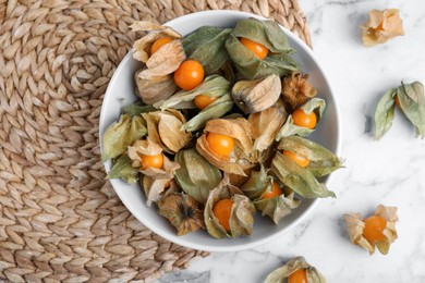 Photo of Ripe physalis fruits with dry husk on white marble table, flat lay