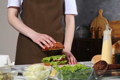 Photo of Woman making delicious vegetarian burger at white marble table, closeup