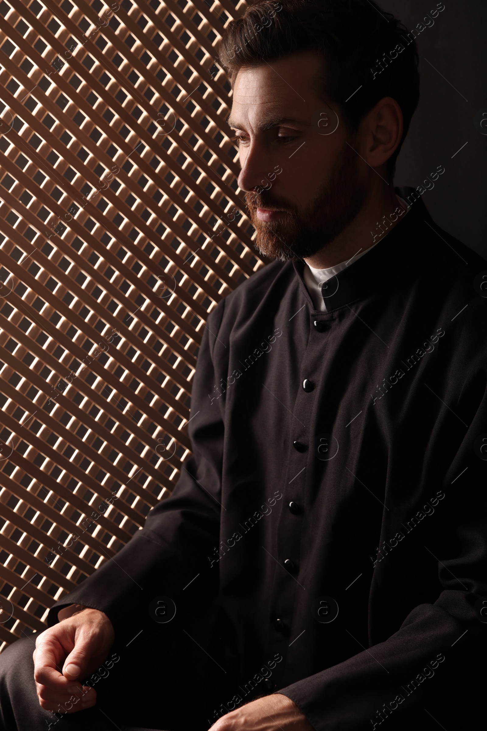 Photo of Catholic priest wearing cassock in confessional booth