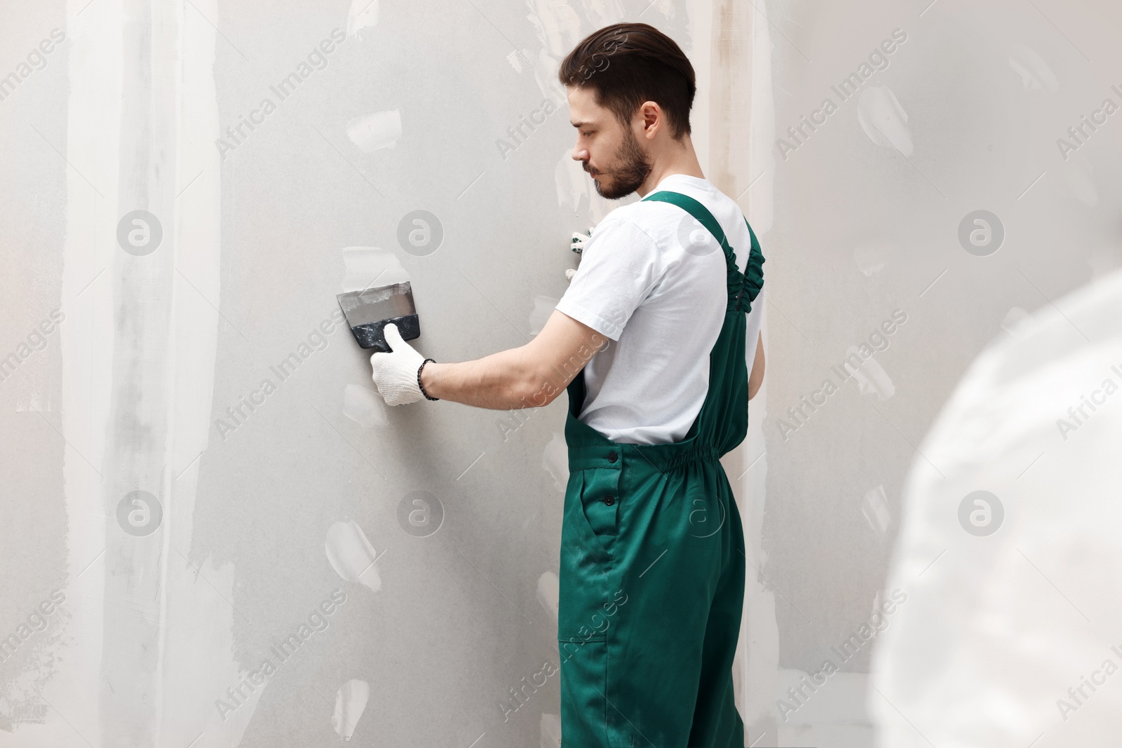 Photo of Worker in uniform plastering wall with putty knife indoors