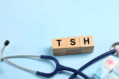 Photo of Endocrinology. Stethoscope, pills and wooden cubes with thyroid hormones on light blue background. Space for text