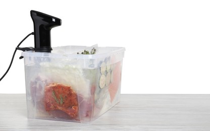 Photo of Sous vide cooker and vacuum packed food products in box on wooden table against white background, space for text. Thermal immersion circulator
