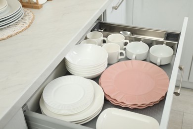 Photo of Clean plates, bowls and cups in drawer indoors