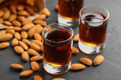 Photo of Glasses with tasty amaretto liqueur and almonds on dark gray table, closeup