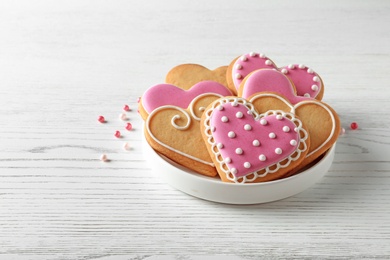 Photo of Plate with decorated heart shaped cookies on wooden table. Space for text