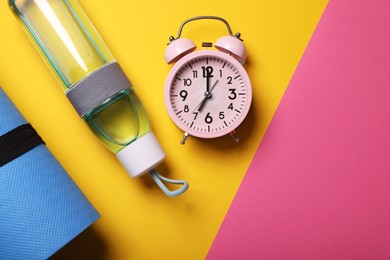 Alarm clock, fitness mat and bottle of water on color background, flat lay with space for text. Morning exercise