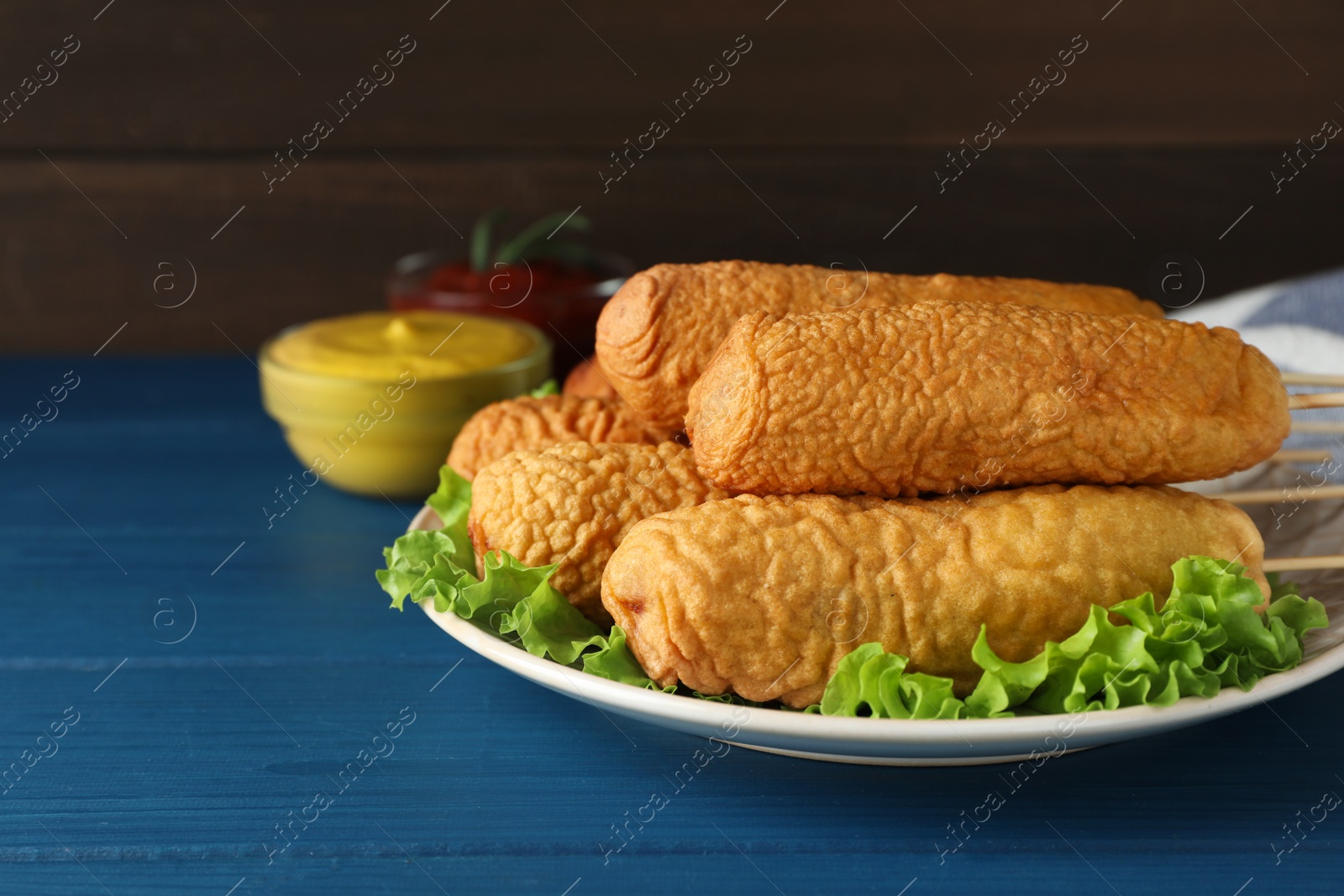 Photo of Delicious deep fried corn dogs and sauces on blue wooden table. Space for text