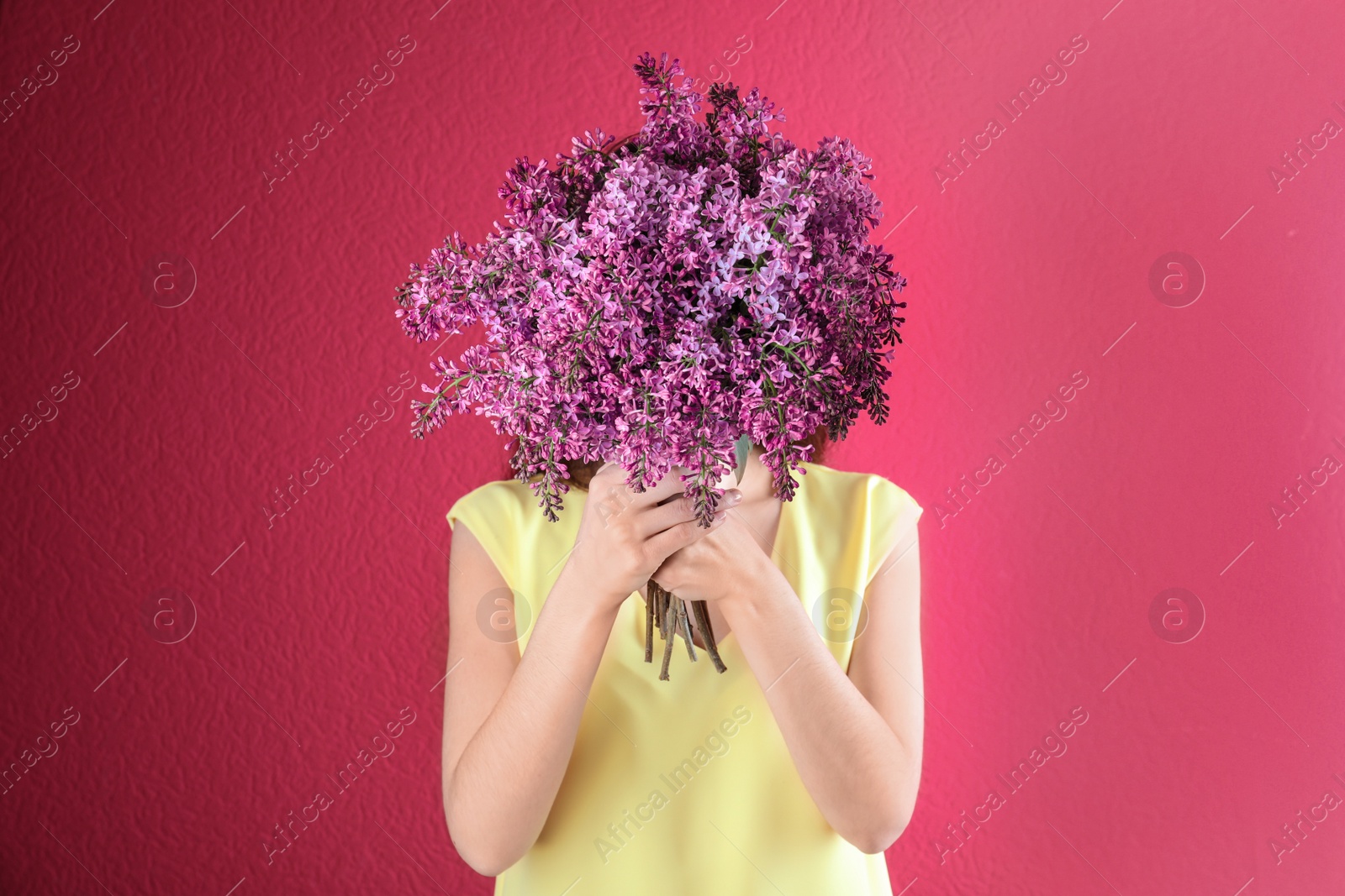 Photo of Woman closing face with bouquet of beautiful lilac flowers on color background