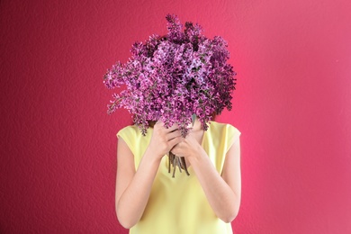 Photo of Woman closing face with bouquet of beautiful lilac flowers on color background