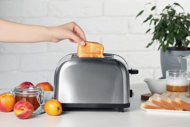 Woman taking roasted bread out of toaster at white table, closeup