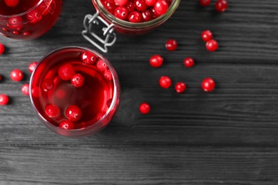 Photo of Tasty cranberry juice in glasses and fresh berries on black wooden table, flat lay. Space for text