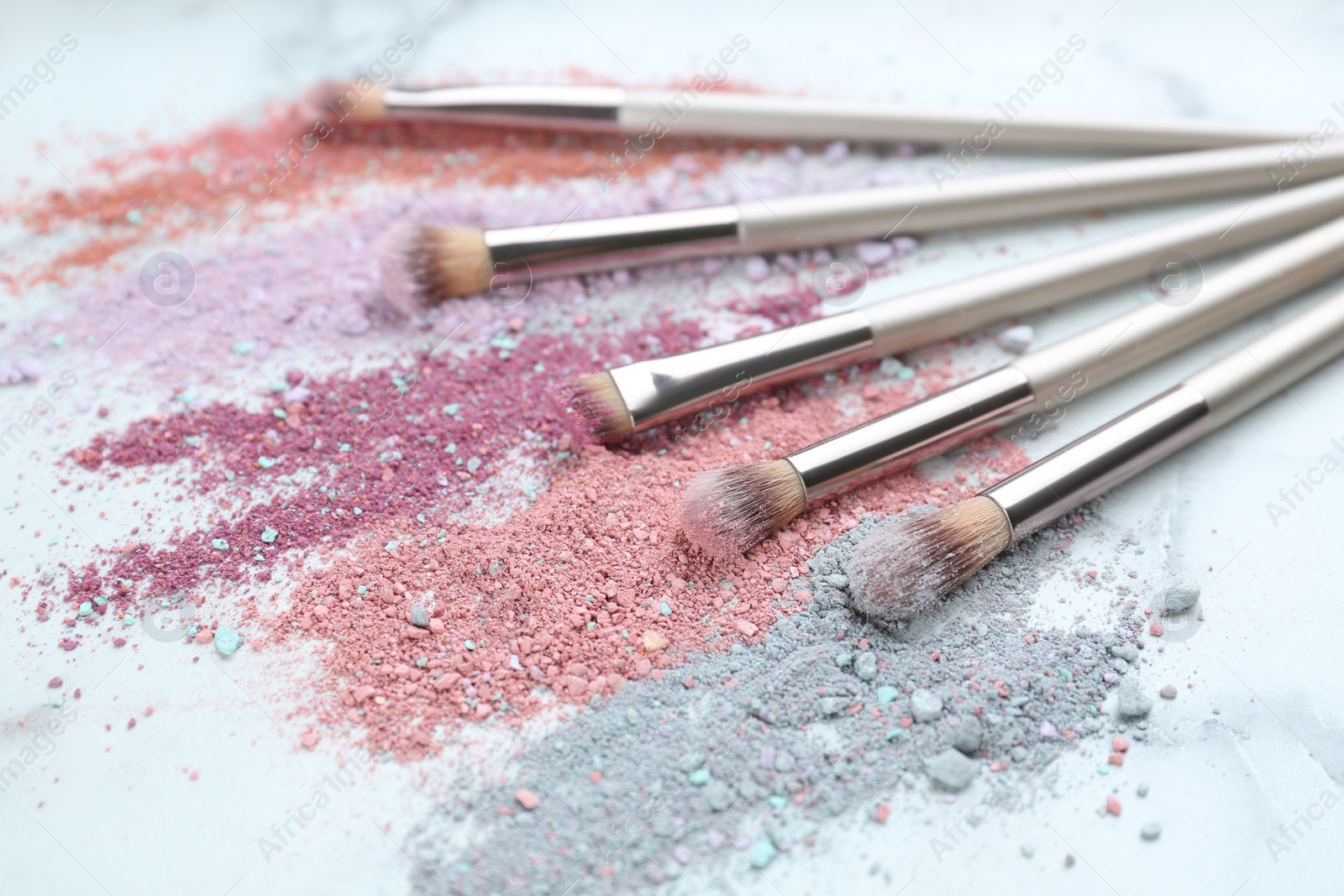 Photo of Different makeup brushes with crushed cosmetic products on white marble table