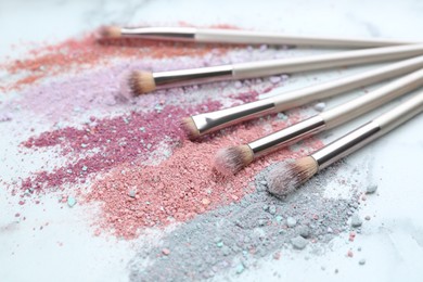 Photo of Different makeup brushes with crushed cosmetic products on white marble table