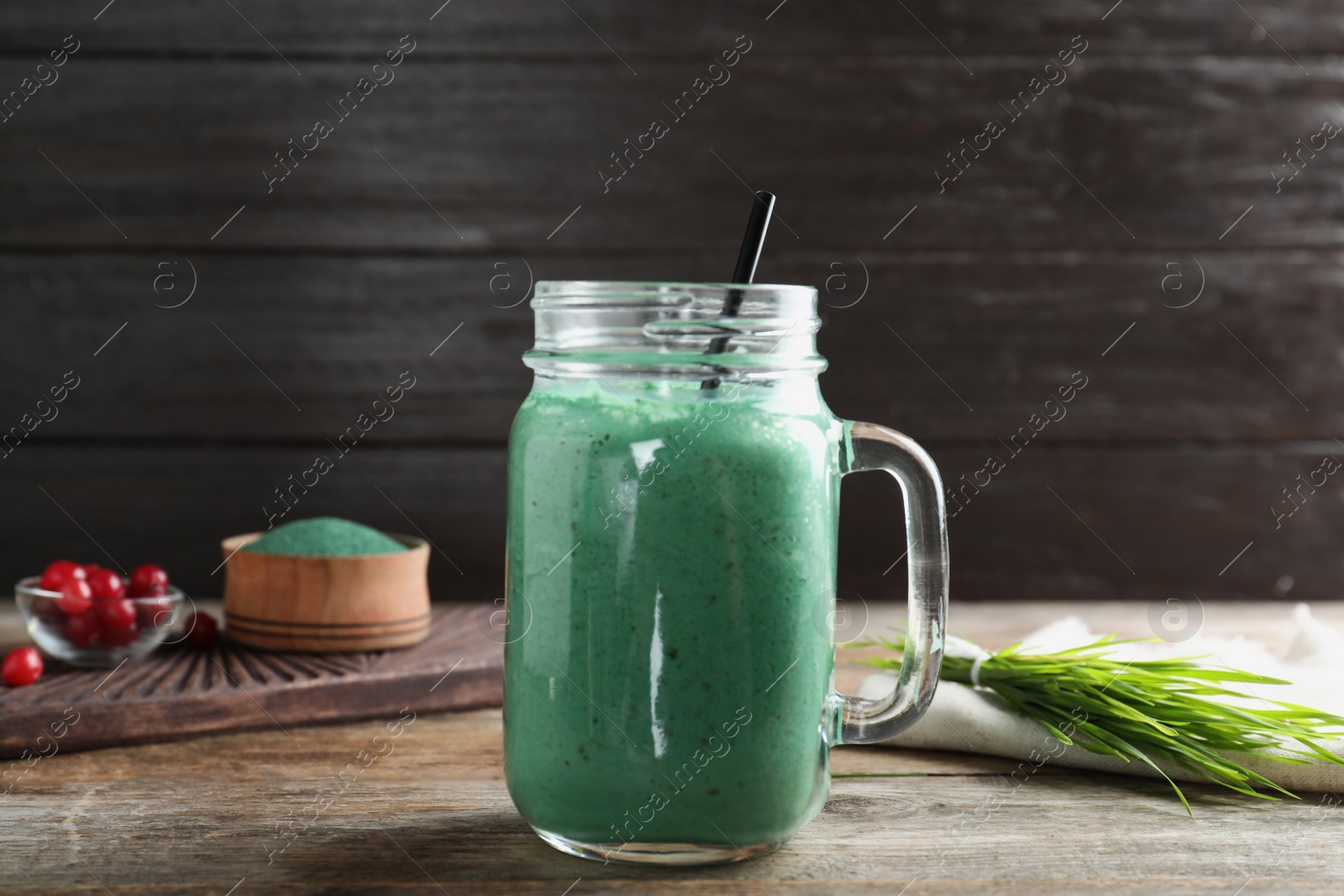 Photo of Mason jar with spirulina smoothie and wheat grass on wooden table