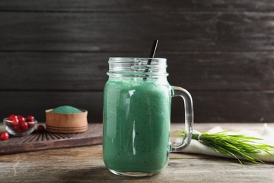 Photo of Mason jar with spirulina smoothie and wheat grass on wooden table