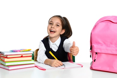 Little girl in uniform doing assignment at desk against white background. School stationery