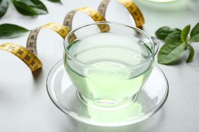 Photo of Cup of herbal diet tea and measuring tape on light table