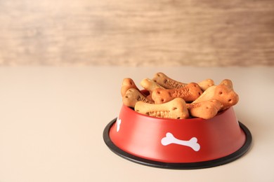 Bone shaped dog cookies in feeding bowl on beige table, space for text
