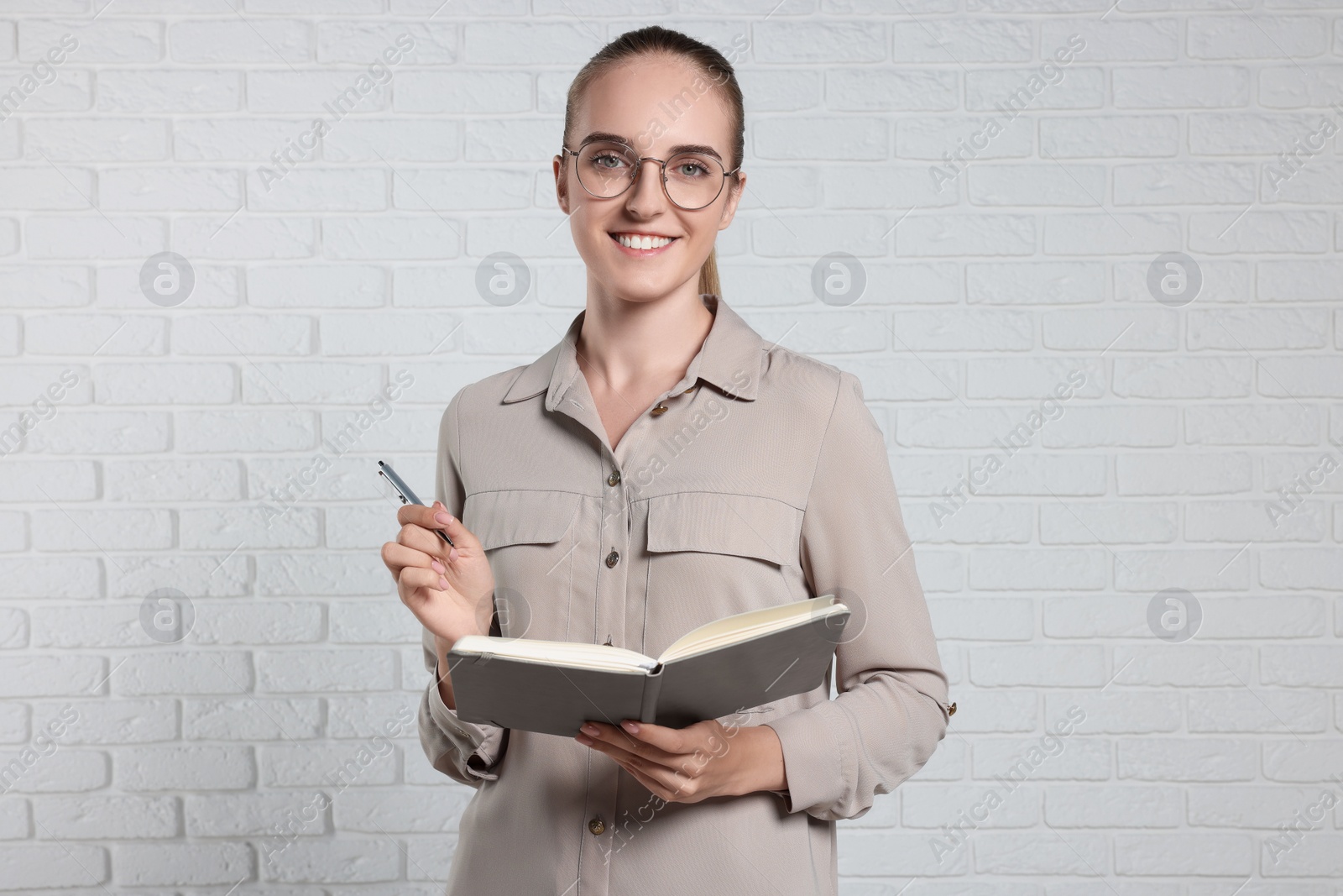 Photo of Happy young secretary with notebook and pen near white brick wall