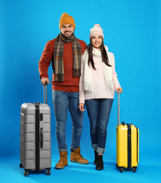 Happy young couple in warm clothes with suitcases on blue background. Winter vacation