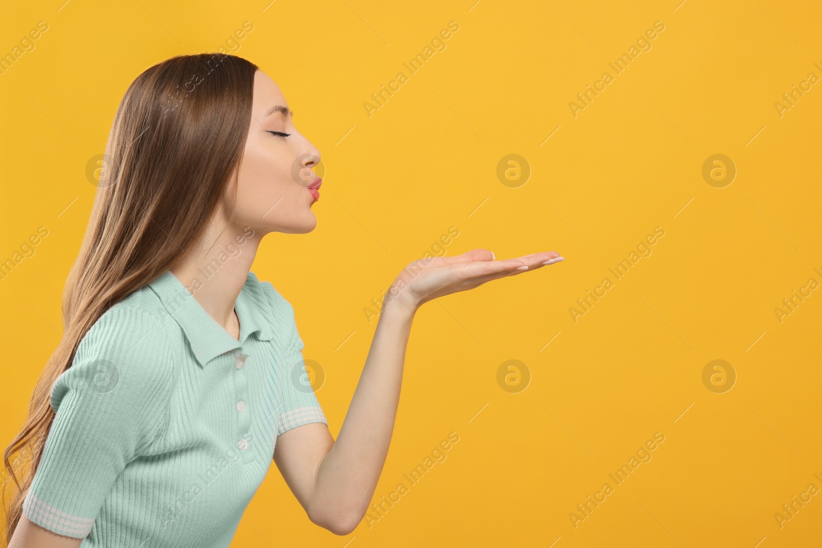 Photo of Beautiful young woman blowing kiss on yellow background, space for text