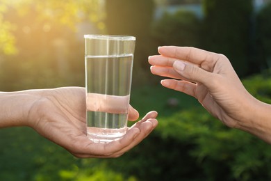 Photo of Man giving glass of fresh water to woman outdoors, closeup