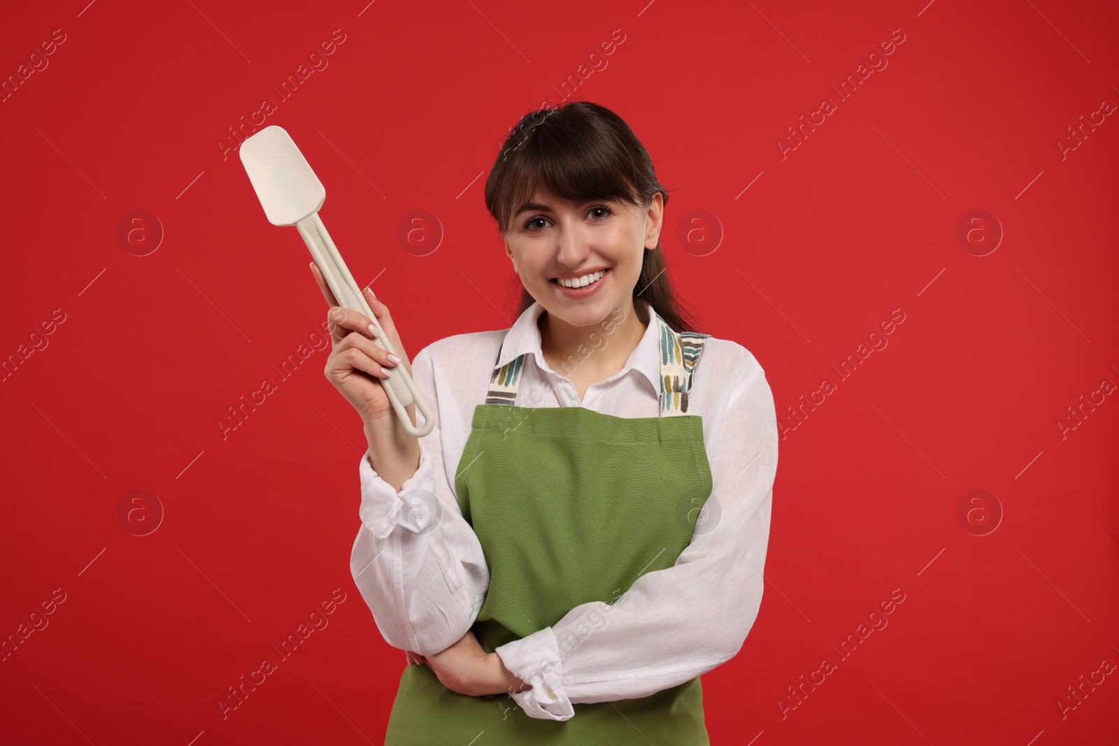Photo of Happy professional confectioner in apron holding spatula on red background