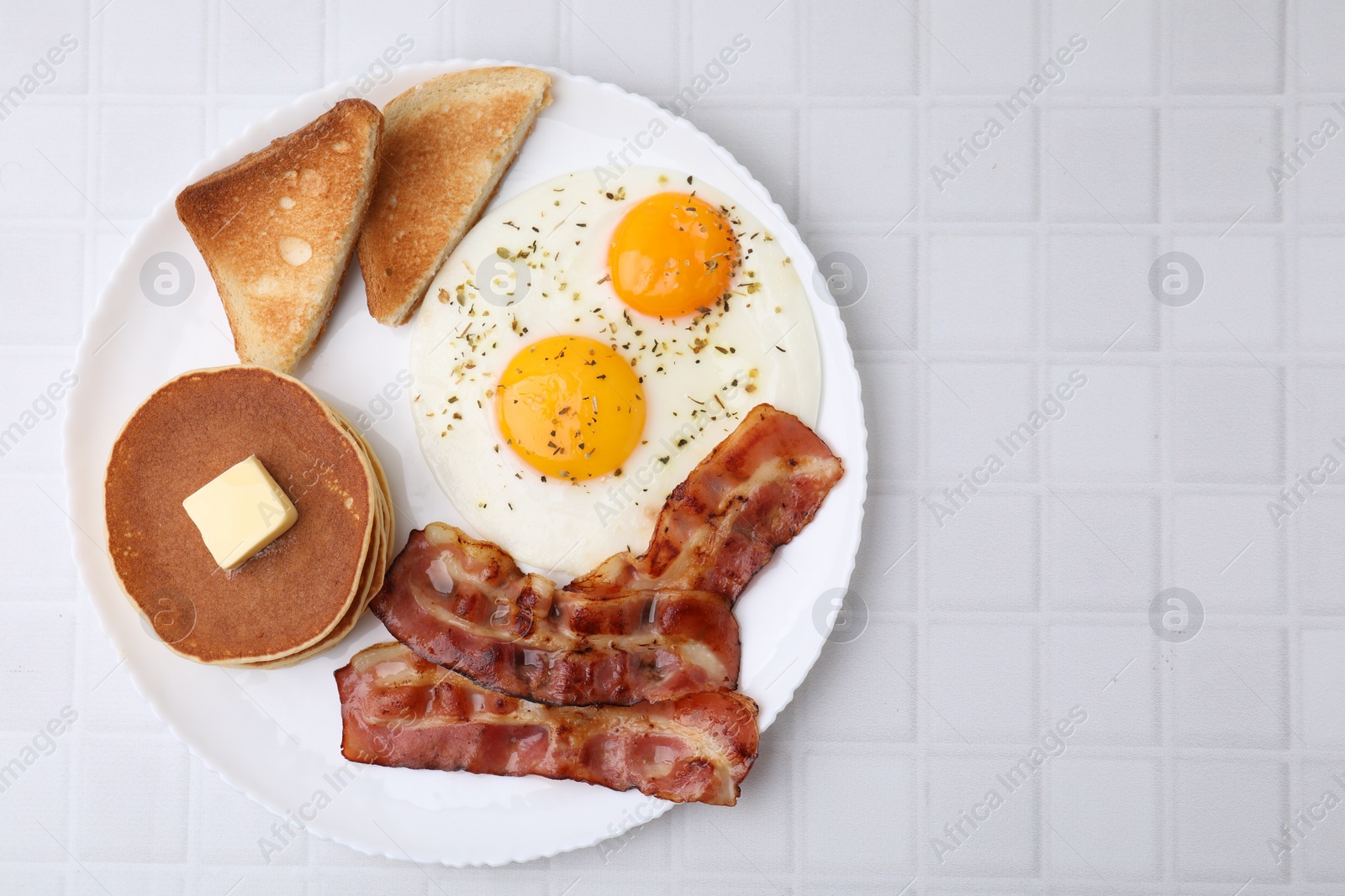 Photo of Tasty pancakes with fried eggs and bacon on white tiled table, top view. Space for text