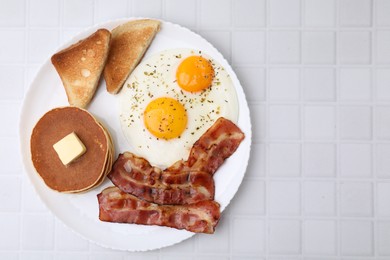 Tasty pancakes with fried eggs and bacon on white tiled table, top view. Space for text