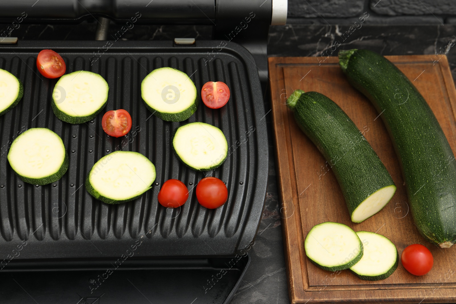 Photo of Electric grill with vegetables on black marble table