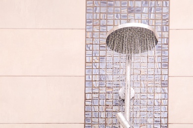 Photo of Shower head with running water in bathroom. Space for text