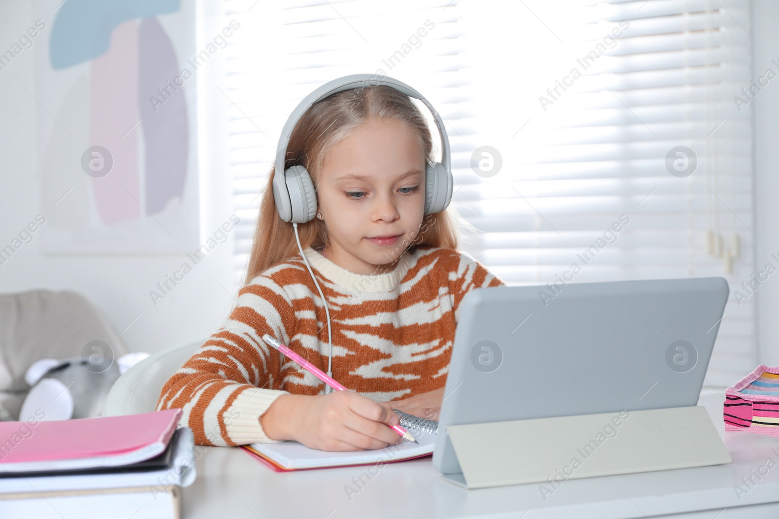 Photo of Cute little girl with modern tablet studying online at home. E-learning