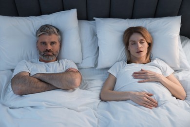 Photo of Irritated man lying near his snoring wife in bed at home