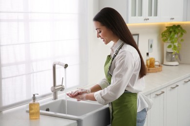 Photo of Young woman washing hands with liquid soap in kitchen